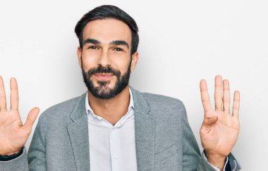 İş kıyafetleri giymiş genç İspanyol bir adam dokuz numarayı gösterip işaret ederken kendinden emin ve mutlu bir şekilde gülümsüyor.. 