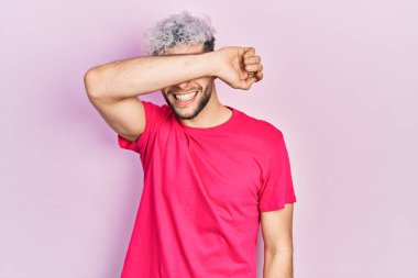 Modern boyalı saçlı, sıradan pembe tişörtlü, gözleri kollarıyla gülen neşeli ve komik bir İspanyol genç. kör kavram. 