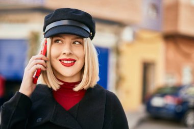 Genç sarışın kadın gülümsüyor. Şehirdeki akıllı telefondan konuşuyor..
