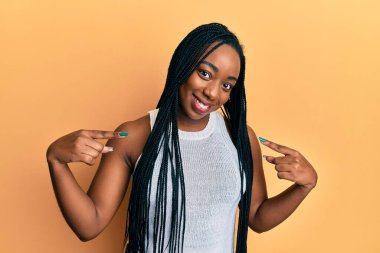 Genç Afro-Amerikan kadın günlük kıyafetler giyiyor. Kendine güvenen, yüzünde gülümseme olan, kendini gururlu ve mutlu bir şekilde gösteren.. 