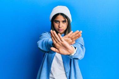 Şirin yün şapkalı genç Latin kadın kollarını kavuşturup, avuç içlerini bozarken, kızgın yüz ifadesi takınıyor. 