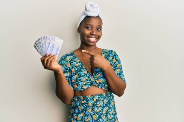 Kıllı türban takan genç Afrikalı bir kadın elinde 20 İsveç banknotuyla mutlu mesut gülümsüyor. 