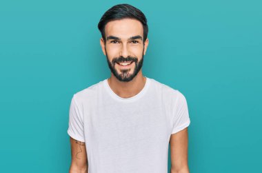 Yüzünde mutlu ve havalı bir gülümseme olan günlük beyaz tişört giyen genç bir İspanyol. şanslı kişi. 