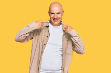 Orta yaşlı, kel, günlük kıyafetler giyen neşeli bir şekilde gülümseyen, parmakları, dişleri ve ağzı olan bir adam. diş sağlığı kavramı. 