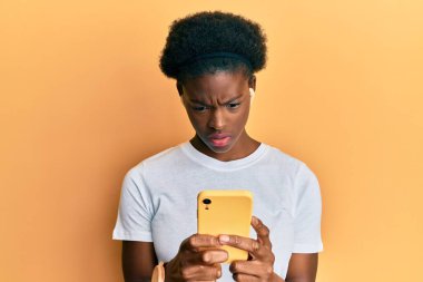 Akıllı telefon ve kulaklık kullanan Afro-Amerikan genç bir kız. Hiçbir şeyden habersiz ve kafası karışmış bir ifade. şüphe kavramı. 