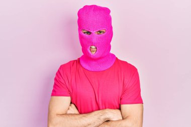 Modern boyalı saçlı, pembe kar maskesi takan, kollarını kavuşturup kameraya gülümseyen genç İspanyol bir adam. pozitif kişi. 