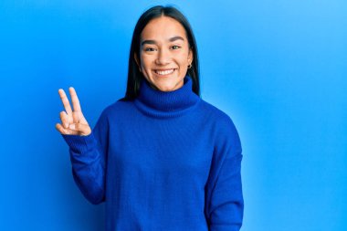 Sıradan bir kazak giyen genç Asyalı kadın kameraya bakıp zafer işareti yapıyor. İki numara.. 