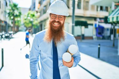 Uzun sakallı, kasketli, mutlu gülümseyen genç bir mimar. Yüzünde tebessümle şehrin planlarını elinde tutarken.