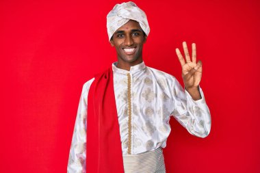 Yakışıklı Hintli adam geleneksel Sherwani sari giysisi giyiyor. Üç numaralı parmaklarıyla gösterip işaret ederken kendinden emin ve mutlu gülümsüyor.. 