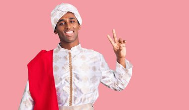 Geleneksel Sherwani elbisesi giyen Afrikalı yakışıklı adam kameraya bakıp zafer işareti yaparken gülümsüyor. İki numara.. 