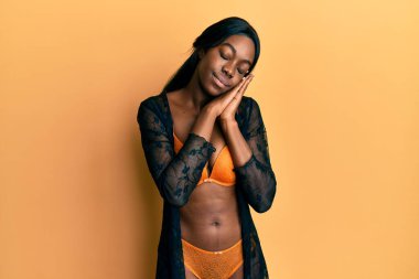 Genç Afro-Amerikalı kadın iç çamaşırı giyip uyuyordu. Yorgundu. Hayal kuruyordu ve elleriyle poz veriyordu.. 