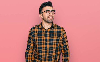 Sakallı, sıradan kıyafetler giyen ve gözlüklü, yüzünde gülümsemeyle yan yana bakan İspanyol bir adam, doğal bir ifade. Kendinden emin gülen. 