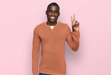 Genç Afro-Amerikalı sıradan kıyafetler giyen, gülen yüzlü, kameraya göz kırpan zafer işareti yapan genç bir adam. İki numara.. 