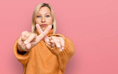 Orta yaşlı beyaz kadın, günlük kışlık süveter giyiyordu. Reddedilme yüz ifadesi, negatif işaret vererek parmaklarını çaprazlıyordu. 