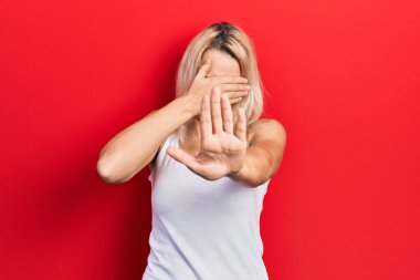 Güzel, beyaz tişört giyen, elleri ve gözleri kapayan, üzgün ve korku dolu hareketler yapan beyaz, sarışın bir kadın. utangaç ve olumsuz kavram. 