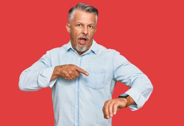 Orta yaşlı, gri saçlı, günlük kıyafetler giyen, acele eden bir adam zamanı, sabırsızlığı ve gecikmeyi işaret ediyor. 