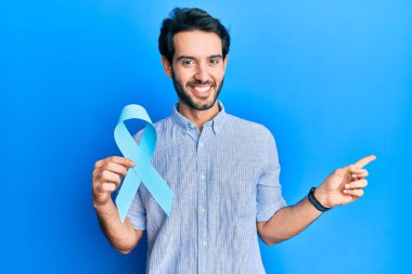 Mavi kurdele tutan genç İspanyol adam gülümsüyor. Mutlu bir şekilde elini ve parmağını yana doğru gösteriyor. 