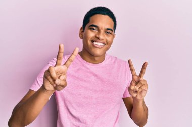 Sıradan pembe tişörtler giyen genç, yakışıklı İspanyol adam kameraya bakıp zafer işareti yapıyor. İki numara.. 