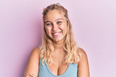 Sıradan kıyafetler giyen, kollarını kavuşturup kameraya bakan mutlu yüzlü genç sarışın kız. pozitif kişi. 