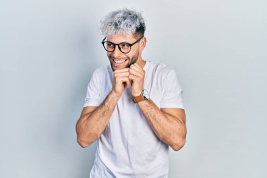 Modern boyalı saçlı, beyaz tişörtlü, gözlüklü, gergin ve heyecanlı genç bir adam. 