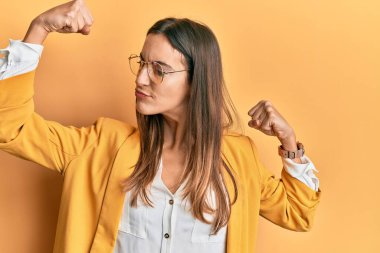 İş tarzı giyinmiş, gözlüklü genç ve güzel bir kadın gururla gülümseyen kol kaslarını gösteriyor. fitness konsepti. 