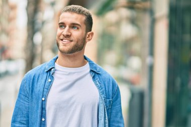 Genç beyaz adam gülümseyerek şehirde mutlu mesut duruyor..