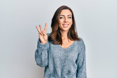 Kış süveteri giyen genç esmer kadın üç numaralı parmaklarını gösterip gülümserken kendinden emin ve mutlu.. 