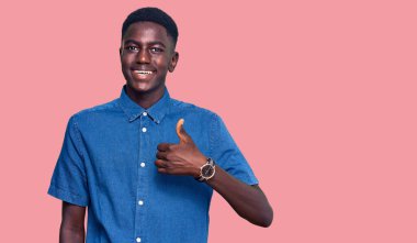 Genç Afro-Amerikan bir adam günlük giysiler giyip mutlu mesut el hareketleriyle selam veriyor. Kameraya bakıp başarıyı gösteren ifade. 