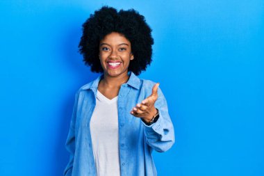 Genç Afrikalı Amerikalı kadın günlük kıyafetler giyip gülümseyerek dostça tokalaşıyor ve hoş geldin diyor. başarılı iş. 