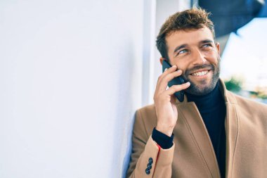 Zarif bir ceket giyen yakışıklı bir iş adamı akıllı telefon kullanarak dışarıda mutlu bir şekilde gülümsüyor.