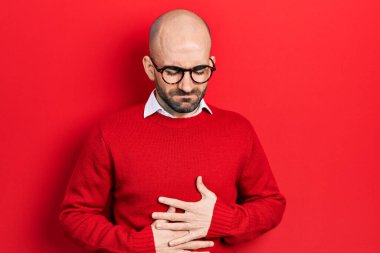 Genç kel bir adam günlük kıyafetler giyiyor ve elleri karnında gözlük takıyor çünkü hazımsızlık, acı verici bir hastalık kendini iyi hissetmiyor. Ağrı kavramı. 