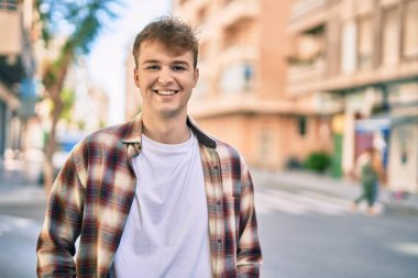 Genç beyaz adam gülümseyerek şehirde mutlu mesut duruyor..