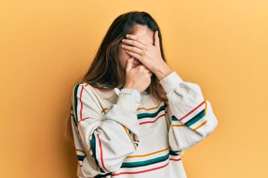 Gündelik giysiler giyen genç beyaz kadın gözlerini ve ağzını elleriyle kapatıyor, şaşırmış ve şok olmuş. duygu gizleme 