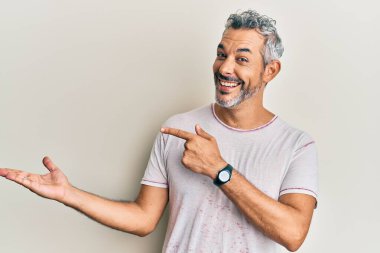 Orta yaşlı, gri saçlı, sıradan kıyafetler giyen bir adam kameraya hayret ediyor ve gülümsüyor.. 