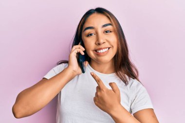 Genç Latin bir kadın akıllı telefondan konuşuyor. Gülümsüyor, mutlu bir şekilde eli ve parmağı işaret ediyor. 