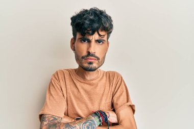 Gündelik kıyafetler giyen, kuşkucu ve gergin genç İspanyol bir adam. Yüzünde çapraz kollarla onaylamayan bir ifade var. negatif kişi. 