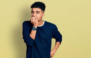 Gündelik kıyafetler giyen genç Afro-Amerikan bir adam gergin görünüyor ve elleri ağzında tırnak yiyor. anksiyete. 