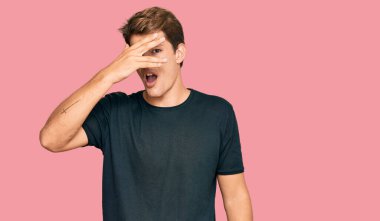 Yakışıklı, beyaz bir adam. Günlük kıyafetler giymiş. Şoka girmiş, yüzünü ve gözlerini kapamış, utanmış ifadesiyle parmaklarından bakıyor.. 