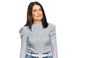 Orta yaşlı esmer kadın günlük kıyafetler giyiyor ve yüzünde ciddi bir ifade var. Basit ve doğal bir şekilde kameraya bakıyorsun.. 