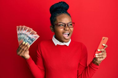 Genç Afro-Amerikalı kadın elinde Avustralya dolarları olan akıllı telefon kullanıyor kızgın ve öfkeli çığlıklar atıyor, öfkeyle bağırıyor. öfke ve agresif konsept. 