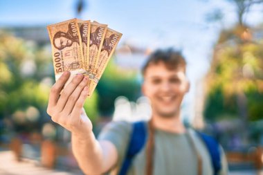 Kafkasyalı genç turist, mutlu bir şekilde gülümsüyor ve şehirde Macar banknotları tutuyor..