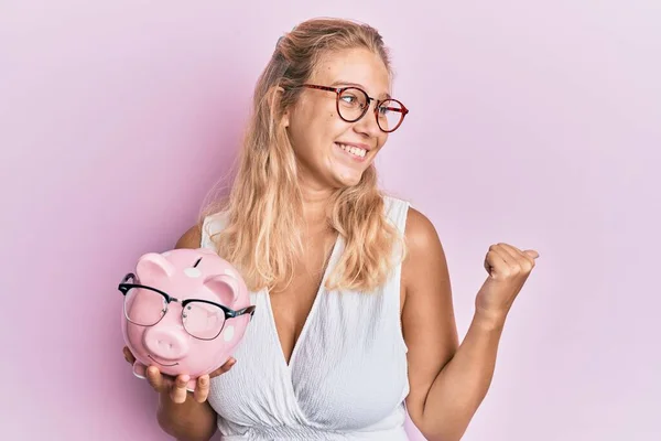 Jong Blond Meisje Holding Piggy Bank Met Bril Wijzen Duim — Stockfoto