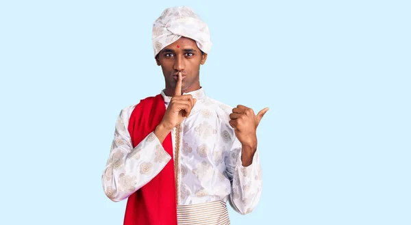 穿着传统雪旺尼酒的非洲帅哥看到衣服要求安静 手指放在嘴唇上 手拉手放在侧面 沉默和秘密概念 — 图库照片