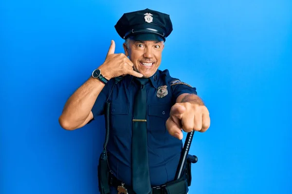 Handsome middle age mature man wearing police uniform smiling doing talking on the telephone gesture and pointing to you. call me.