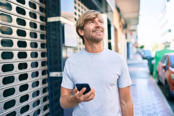 英俊的高加索男人在户外用智能手机开心地笑着 — 图库照片