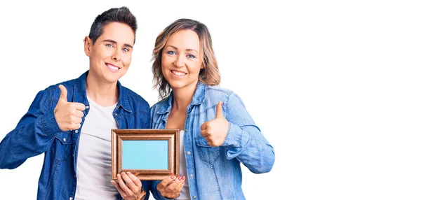Couple Women Holding Empty Frame Doing Happy Thumbs Gesture Hand — Stock Photo, Image