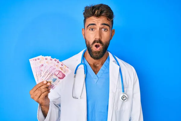 Joven Hombre Hispano Vistiendo Uniforme Médico Sosteniendo Pesos Mexicanos Asustado — Foto de Stock