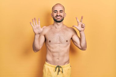 Mayolu genç kel bir adam 8 numarayı gösterip işaret ederken kendinden emin ve mutlu gülümsüyor.. 