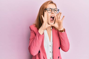 İş stili ve gözlük takan genç beyaz kadın elleri ağızda bağırarak bağırıyor. 