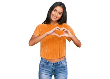 Genç esmer Arap kadın gündelik giysiler giyiyor, aşıkken gülümsüyor, elleriyle kalp sembolü yapıyor. romantik kavram. 